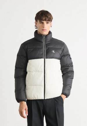 Giacca imbottita con la parte superiore nera e la parte inferiore crema, caratterizzata da un colletto alto, zip frontale e polsini elasticizzati. Logo CK sul petto.