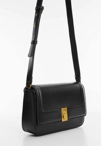 Musta nahkainen käsilaukku, jossa on jäsennelty muoto, kultaisen sävyinen lukko ja säädettävä hihna, sileä pinta ja minimalistiset design-elementit.