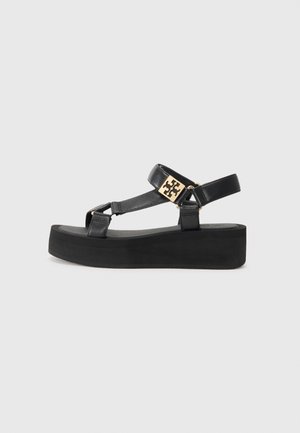 Black leather sandals with a platform sole. Features include a T-strap design, adjustable ankle strap, and gold-tone hardware detail.