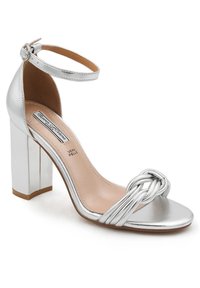 Sandal con tacco a blocco in argento, con cinturino alla caviglia e dettagli intrecciati sulla punta. Realizzata in pelle con una texture liscia.