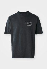 T-shirt en coton noir à manches courtes, avec un col rond, et un texte graphique blanc indiquant "OBEY" et "movement" sur la poitrine.