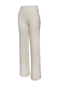 Beige weit geschnittene Hose aus weichem Stoff, mit einem elastischen Bund und einem bedruckten Logo an dem linken Bein. Glatte Textur und bequemer Sitz.