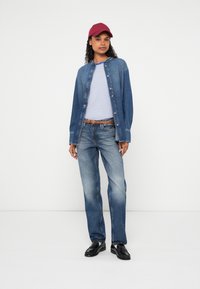 Τζιν μπουφάν με κουμπιά, λευκό και μπλε ριγέ t-shirt, μπλε τζιν, καφέ ζώνη και μπορντό καπέλο· μαύρα παπούτσια ολοκληρώνουν την εμφάνιση.