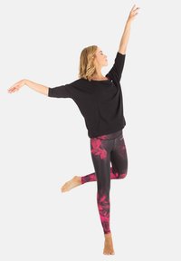 Black loose-fitting top with draped neckline, paired with form-fitting leggings featuring red and pink geometric patterns.