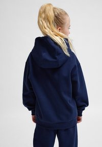 Marinblå huvtröja med en avslappnad passform, ribbade ärmslut och nederkant, gjord av mjukt material. Har en stor huva och minimal detaljering.