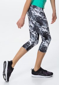 Leggings con un motivo floreale in bianco e nero, realizzati in materiale elasticizzato, con una lunghezza cropped e cuciture piatte. Abbinati a scarpe da ginnastica nere.