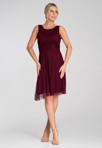 Burgunderfarbendes, ärmelloses Kleid mit tailliertem Oberteil, gerafftem Bund und fließendem Rock. Glatter Stoff mit einem transparenten Überzug am Saum.