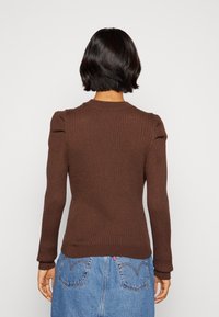 Brauner, gerippter Pullover mit puffigen Ärmeln, tailliertem Schnitt und rundem Ausschnitt. Getragen mit einem Jeansrock, der den strukturierten Stoff zeigt.