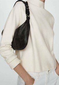 Pull créme à col montant, associé à un sac à épaule en cuir texturé foncé avec une forme incurvée et des accessoires en métal.