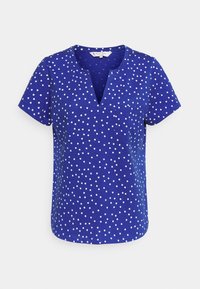 Blue short-sleeve top featuring a V-neck, made from a textured fabric, adorned with white polka dots throughout. Casual design with a relaxed fit.