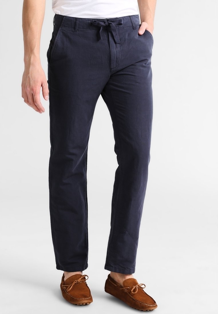 Homme portant un pantalon bleu marine foncé coupe décontractée avec une taille à cordon et des mocassins en daim marron.