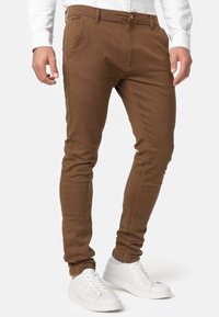 Brune slim-fit bukser lavet af struktureret stof. Har en knaplukning, sidelommer og er parret med hvide sneakers.