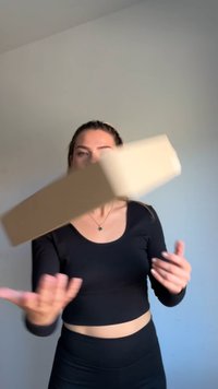 Šviesiai rudas stačiakampis dėžė laikoma virš žmogaus rankų, su lygiu paviršiumi ir suapvalintais kampais, prieš šviesiai pilką foną.