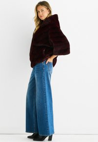 Burgundy faux fur cropped jacket with wide sleeves and a high collar, paired with high-waisted blue wide-leg jeans and black high-heeled boots.