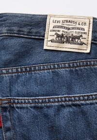 Denimová látka v tmavě modré barvě s texturovaným povrchem. Obsahuje bavlněnou nálepku s nápisem "Levi Strauss & Co." a ilustrací a datem.