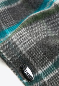 Écharpe en laine grise et bleue canard présentant un motif à carreaux, avec une étiquette de marque argentée attachée, texture douce avec une apparence légèrement floue.