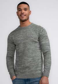 Gray knit sweater with a textured pattern, round neckline, and ribbed cuffs. Worn with blue denim jeans, showing a casual style.