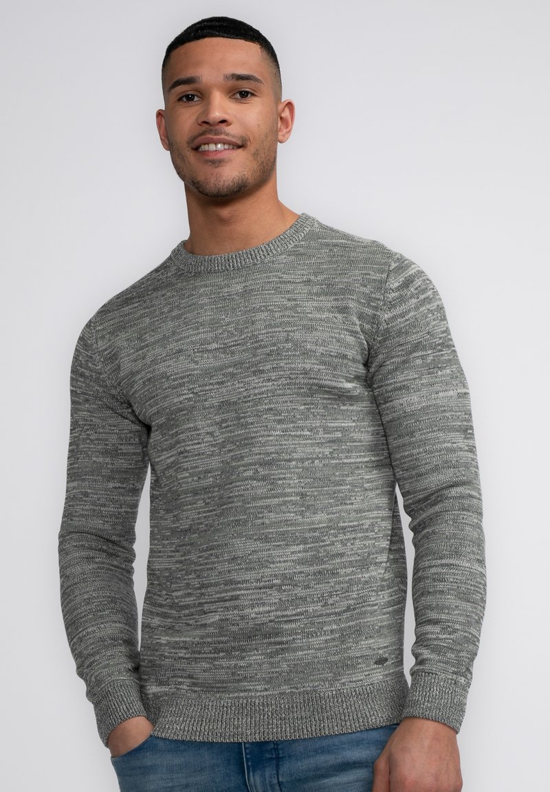 Gray knit sweater with a textured pattern, round neckline, and ribbed cuffs. Worn with blue denim jeans, showing a casual style.