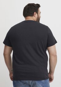 Sort bomulds T-shirt med korte ærmer, rund halsudskæring og en afslappet pasform, vist fra ryggen på en person iført blå jeans.