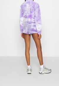 Purple tie-dye hoodie and shorts set with "Juicy" in rhinestones on the back. Paired with silver athletic shoes. Smooth fabric texture.