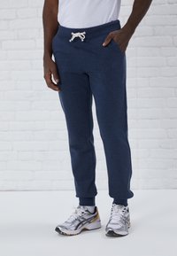 Pantalons de survêtement bleu marine avec une taille à cordon, poches latérales et chevilles resserrées, assortis à des chaussures de sport argentées et dorées.