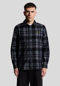 Camisa de franela negra y gris con patrón de cuadros, diseño de botones, acentos en azul y blanco en contraste, y un pequeño logo amarillo en el pecho.
