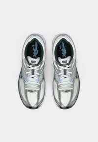 Zapatillas de running Nike en plata y blanco con parte superior de malla, collar acolchado y logotipo característico. Los cordones son azul claro con detalles en gris.