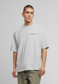 Tricou supradimensionat gri, din bumbac, cu mâneci scurte și gât rotund. Inscripția „PROHIBIT” imprimată în roșu pe pieptul stâng.