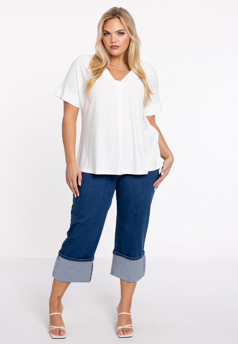 Hvid, kortærmet V-hals top parret med mørkeblå cropped jeans med lys denimmanchetter. Modellen bærer hvide strop sandaler.