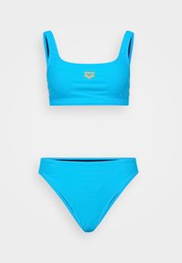Mėlynas bikini rinkinys, kuriame yra kvadratinio apykaklės viršus su plačiomis petnešomis ir atitinkančios žemos juosmens kelnaitės, pagamintos iš glotnios ir tamprios medžiagos. Auksinis logotipo akcentas.