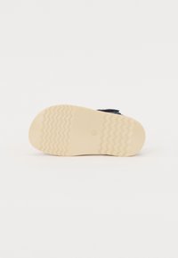 Suela de zapato con material de goma texturizada en color crema. Presenta un patrón en zigzag para tracción y una forma plana y redondeada.