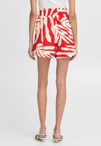 Shorts rouges et crème à motifs avec une taille haute et des jambes larges, fabriqués dans un tissu léger, présentant de grands motifs de feuilles.