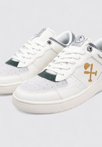 Zapatillas blancas de cuero con detalles en gris y verde, con puntera perforada, detalles de ante y un logo dorado en el lateral.