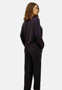 Ensemble haut à manches longues et pantalon en tissu violet foncé, présentant une coupe décontractée et une texture douce, avec des coutures minimales et sans motifs visibles.