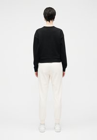 Μαύρο φούτερ με χαλαρή εφαρμογή στους ώμους, με λεία υφή, συνδυασμένο με κρεμ παντελόνι jogger, με ριμπ μανσέτες και λευκά αθλητικά παπούτσια.