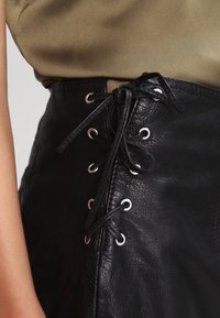 Svart läderkjol med snörning framtill och silverfärgade öglor. Slät textur, figursydd design och hög midja.