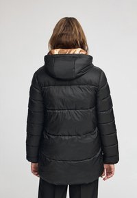 Czarna pikowana kurtka z kapturem, z poziomymi przeszyciami. Wnętrze podszewki ma kontrastujący brązowy kolor.