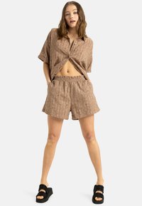 Brun mönstrad kortärmad skjorta med knapplist i kombination med matchande shorts, som har resårmidja. Bärs med svarta plattformssandal.