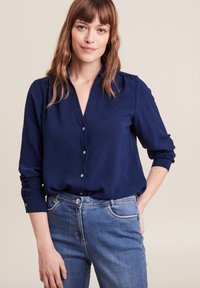 Marineblauwe button-up shirt met lange mouwen, textuurstof, subtiele glans en lichtblauwe knopen, gecombineerd met blauwe denim jeans.