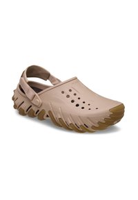 Lichtroze plastic klompen met een gesloten neus, uitgesneden ventilatiegaten en een gestructureerde, golvende beige rubberschoenzool; verstelbare hakriem.