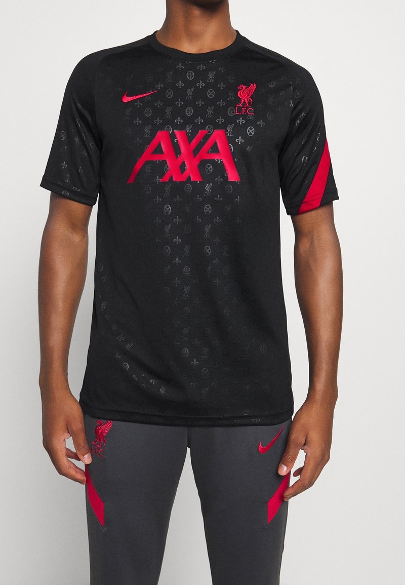 Černé sportovní tričko Nike s červeným logem „AXA“, znakem Liverpoolu a tónovaným vzorem; krátké rukávy s červenými detaily. Spárováno s šedými kalhotami.