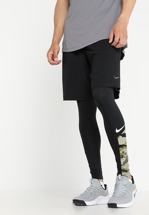 Czarne sportowe szorty na tle czarnych legginsów w wzór kamuflażu, w połączeniu z szarymi trampkami. Górna część to luźna szara koszulka.