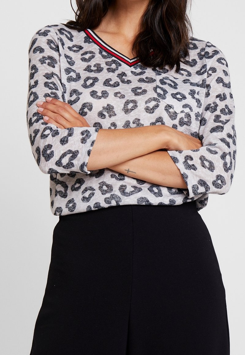 Haut à imprimé léopard en gris clair avec motifs noirs, col en V avec rayures rouges et noires, manches trois-quarts et coupe décontractée.