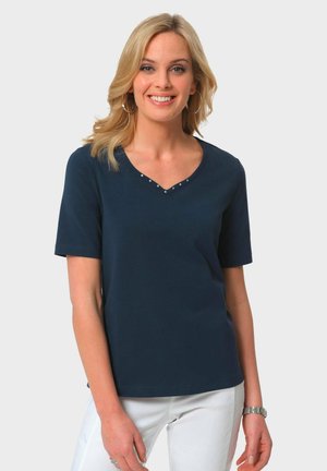 Maglietta a V blu navy in tessuto morbido con maniche corte. Presenta borchie decorative lungo il scollo.