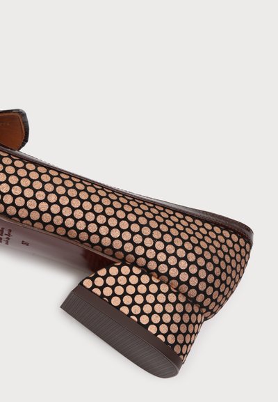 Gros plan d'une chaussure marron à talon bas avec un motif de points bronze brillants uniformément espacés sur la tige et le talon.