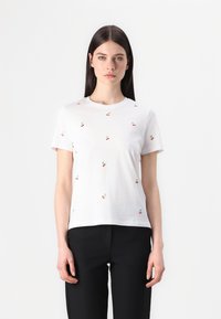 Witte katoenen t-shirt met kleine rode kers borduursels. Korte mouwen, ronde hals, relaxed fit. Combinatie met zwarte broek.