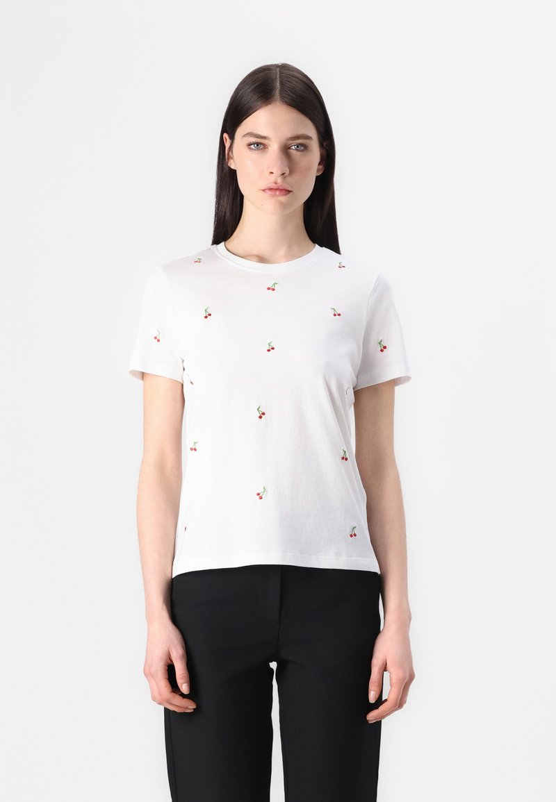 Witte katoenen t-shirt met kleine rode kers borduursels. Korte mouwen, ronde hals, relaxed fit. Combinatie met zwarte broek.