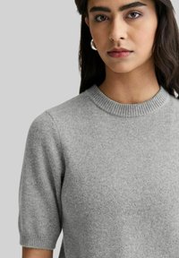 Lys grå kortærmet sweater med ribbet rund Hals. Lavet af blødt materiale med en subtil tekstur, som har let udblæste ærmer.