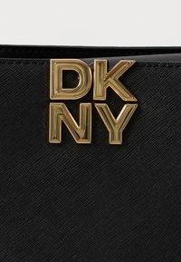 Μαύρη υφασμάτινη τσάντα με χρυσό λογότυπο "DK NY" μπροστά. Το υλικό έχει ένα διακριτικό σχέδιο, ενισχύοντας την οπτική του απήχηση.