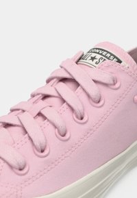 Baskets Converse All Star en toile rose clair avec des lacets assortis, des œillets en métal et une semelle en caoutchouc blanche.